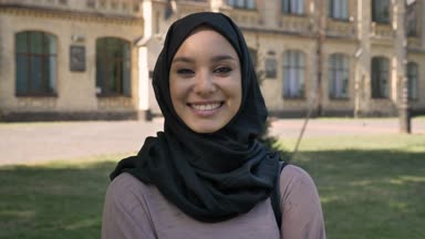 Hijab genç güzel Müslüman kız gülümseyerek ve yaz aylarında gündüz kameraya, izlerken arka planda, religiuos kavram bina kıkırdayarak