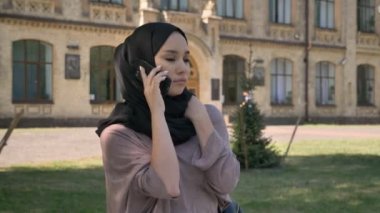 Genç Müslüman kıza hijab telefonda konuşurken ve Bina arka plan, religiuos kavramı, iletişim kavramı üzerinde yaz aylarında gündüz gülüyor
