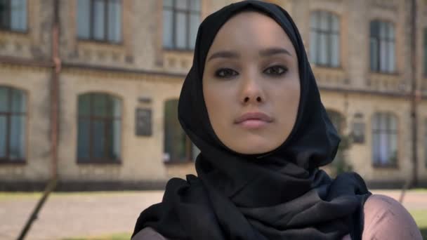 Young self-confident muslim girl is watching at camera in daytime in summer , building on background, religious concept — Stock Video