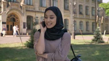 Genç Müslüman kıza hijab telefon ve el yaz aylarında gündüz Bina arka plan, religiuos kavramı, iletişim kavramı üzerinde konuşuyor