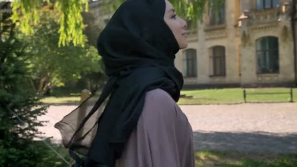 Mladá sladká muslimská dívka v hidžábu se usmívá a jít na univerzitu v Délka dne v létě, náboženské pojetí, studovat koncepce, boční pohled — Stock video