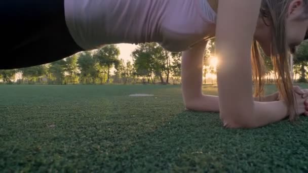 Dos mujeres jóvenes haciendo ejercicio de tablón en el campo en el parque durante el atardecer, modelos de fitness haciendo ejercicio — Vídeo de stock