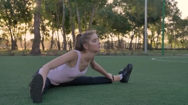 Mujer bonita joven que se extiende en el campo de fútbol en el parque, entrenamiento de la mañana, ejercicio de modelo de fitness — Vídeo de stock