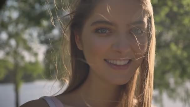 Portret van jonge mooie vrouw kijken in de camera en lachend, blij, park in de buurt van rivier achtergrond — Stockvideo