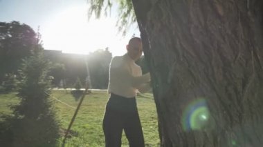 Genç olağanüstü mutlu kalın kız ağacın arkasına saklanarak ve çimenlerin üzerine Park ışığında, yaz aylarında flört anlayışı