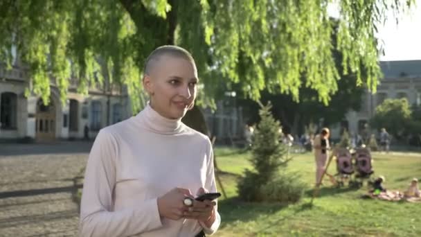 Genç olağanüstü cesur kız gün ışığında, parkın içinden yaz aylarında mesaj yazarak smartphone, iletişim kavramı, düşünme kavramı üzerinde yürüyor — Stok video