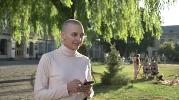 Joven extraordinaria chica audaz está caminando a través del parque a la luz del día, en verano, escribiendo mensaje en el teléfono inteligente, concepto de comunicación, concepto de pensamiento — Vídeo de stock