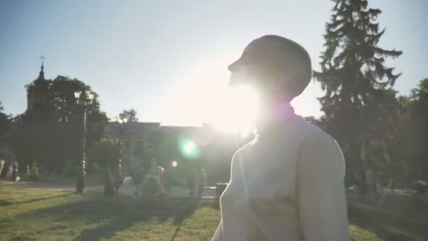 Молода надзвичайно смілива дівчина ходить в парку, обертається навколо, захищаючись від сонця, думаючи концепцію, вид збоку — стокове відео