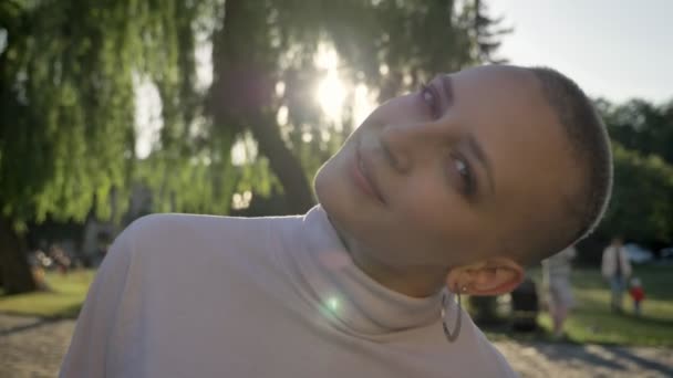 Joven chica feliz extraordinaria abre los ojos en el parque a la luz del día en verano, mira a la cámara, sonríe, concepto de ensueño, concepto de coqueteo, fondo borroso — Vídeos de Stock