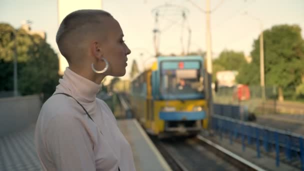 Jeune fille extraordinaire audacieuse regarde comment le train arrive sur la gare de jour en été, marche, concept urbain, vue latérale — Video