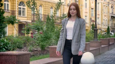 Kendine güvenen genç kadın caddesi şehrin ve sarı binanın arka plan etrafında, seyir aşağı yürüyüş ceketli zencefil