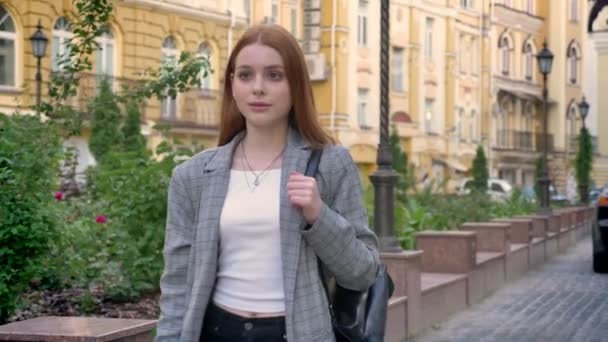 Молода впевнена жінка з імбирним волоссям, що йде по місту і з нетерпінням чекає, жовтий будівельний фон — стокове відео