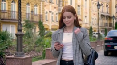 Şehirde yürüyüş ve seyir onun telefon, arka bina sarı Kızıl saçlı Genç güzel kadın