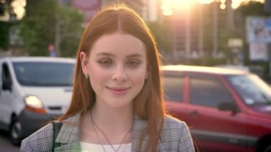 Sokakta duran ve kamera seyir günbatımı, gülümseyen, araba arka plan trafik sırasında Kızıl saçlı Genç güzel kadın