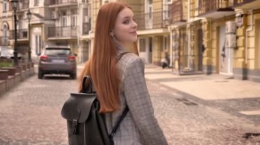 Şehir sokak üzerinde yürüme ve geriye dönüp baktığımda, holding sırt çantası, kentsel sokak arka plan, arkadan görünüm uzun kızıl saçlı Genç kadın