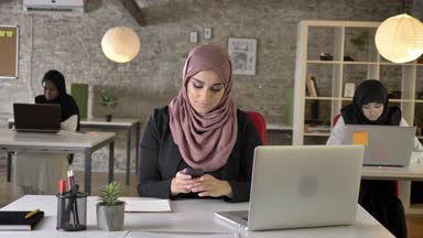 Üç genç Müslüman kadının içinde oturan ve modern ofis, çok kadın işçi telefonla yazmaya çalışan Hicap