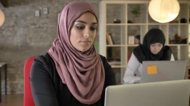 Çalışma, ciddi, genç Müslüman kadınların içinde oturan ve modern ofis, dizüstü bilgisayarda yazarak hijab iki kadın portre konsantre