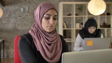 Çalışma ve kamera, oturma ve modern ofis dizüstü bilgisayarda yazarak iki bayan arıyorum hijab genç Müslüman kadın portresi