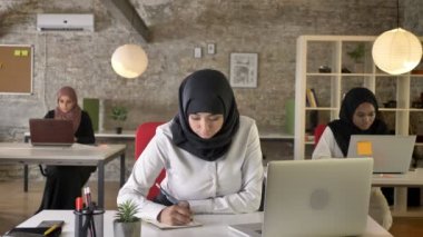 Üç genç Müslüman kadın içinde oturan ve modern ofis, kağıda, yazı çok kadın işçi çalışan hijab meşgul