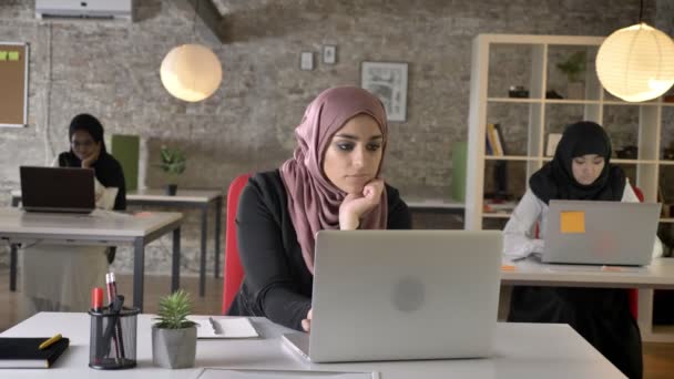 Tres jóvenes musulmanas en hiyab sentadas y trabajando en una oficina moderna, hermosa mujer musulmana bostezando, exhausta — Vídeos de Stock
