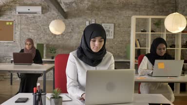 Üç genç Müslüman kadın içinde oturan ve laptop modern ofis içinde öksürük ve çalışma hasta kadın yazarak türban