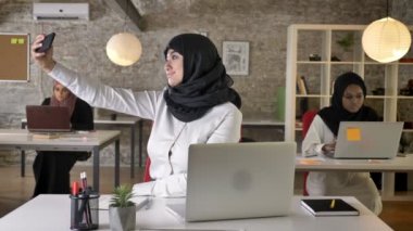 Üç genç Müslüman kadın oturuyor ve modern ofis, selfie telefon ile çekici güzel Müslüman kadın çalışan hijab içinde gülümseyen