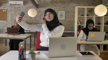 Diğer Müslüman kadın almak selfie ile smartphone ise modern ofis çalışma hijab içinde üç genç Müslüman kadın