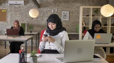 Üç genç Müslüman kadın içinde oturan ve kadın işçi manifatura telefon büyüleyici laptop modern ofisindeki yazarak türban