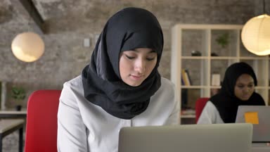 Çalışma ve kamera seyir, gülümseyen, modern ofisinde oturan iki kadın Tesettür genç Müslüman kadın portresi
