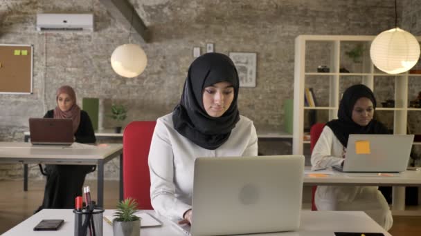 Tiga perempuan muslim muda dalam hijab duduk dan mengetik di laptop di kantor modern, wanita sakit batuk dan bekerja — Stok Video