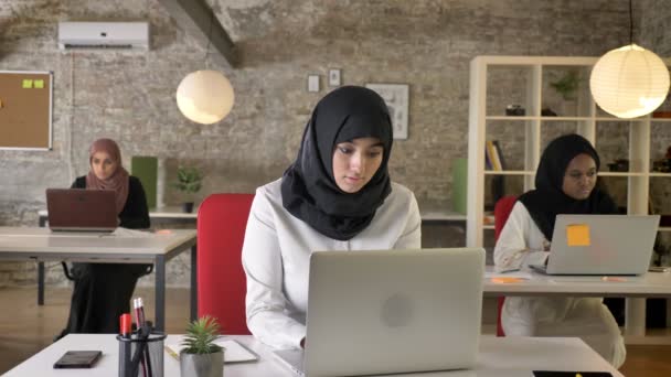三年轻的穆斯林妇女在面纱坐和工作在膝上型电脑在现代办公室, 穆斯林妇女打呵欠, 疲倦 — 图库视频影像