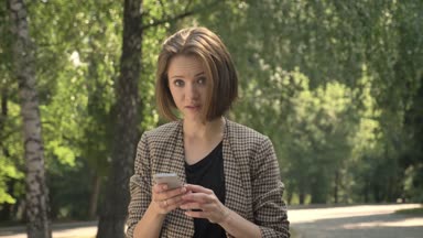 Genç sürpriz kız parkta smartphone içinde gündüz, yaz aylarında, kameraya, iletişim kavramı izlerken izliyor