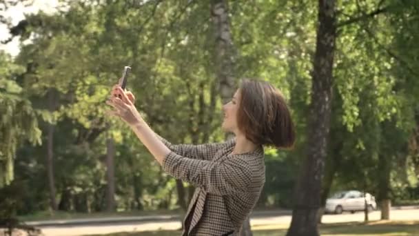 Young attractive girl is making selfie in park in daytime, duck face, in summer, communication concept, side view — Stock Video