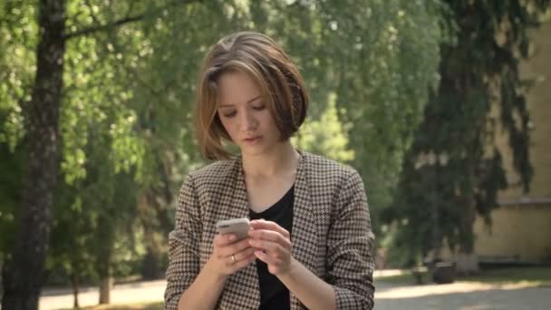 魅力的な濃縮された少女は夏 通信の概念に 昼間公園でスマート フォンでメッセージを入力します — ストック動画