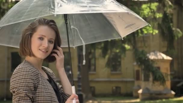 Aantrekkelijk meisje loopt in park met paraplu overdag, in de zomer, lacht, kijken op camera — Stockvideo