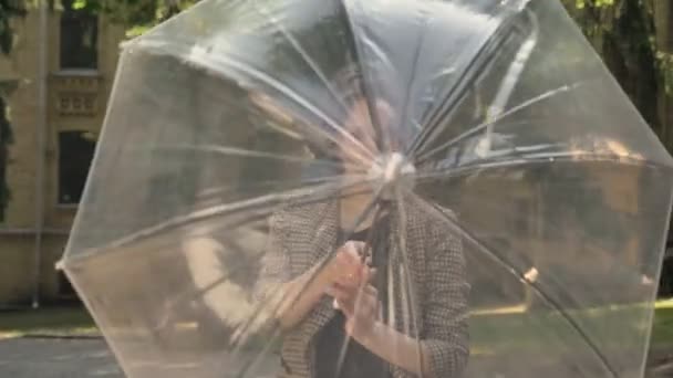 Молодая привлекательная девушка открывает и крутит зонтик в парке днем, летом, наблюдая за камерой — стоковое видео