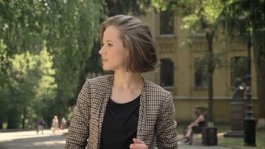 Genç güzel mutlu kız parkta gündüz yaz, kameraya izlerken duruyor