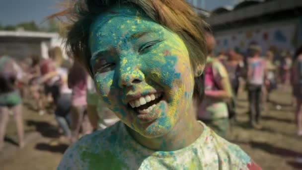Joven chica asiática feliz está sonriendo y guiñando el ojo con polvo colorido en el festival holi en el día en verano, concepto de color, concepto de coqueteo — Vídeo de stock