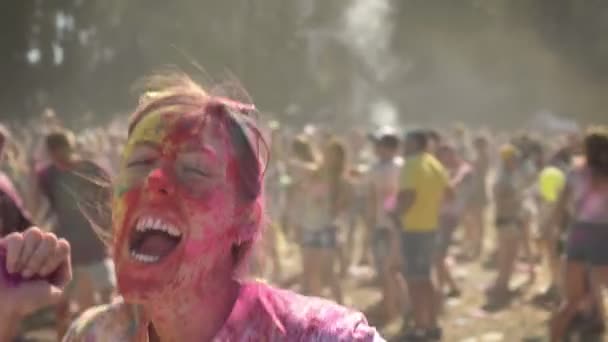 Joven chica animada en polvo colorido está saltando y bailando en el festival de holi durante el día en verano, concepto de color, concepto emocional — Vídeos de Stock