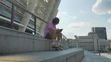 Genç adam hipster mesaj yazarak smartphone, kaykay, kentsel kavramı, iletişim kavramı, yan görünüm