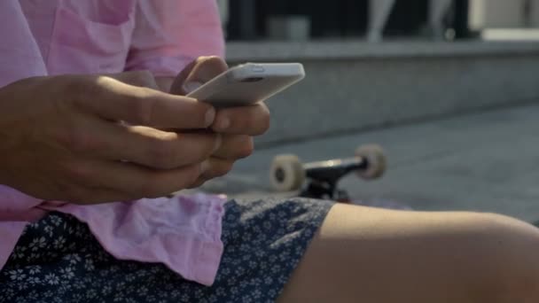 Hipster вводить повідомлення на смартфон, скейтборд, розмитий фон, міську концепцію, концепцію комунікації — стокове відео