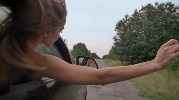 Silhouette di giovane bella ragazza mette testa e mano fuori dal finestrino dell'auto durante la corsa, concetto trevel — Video Stock