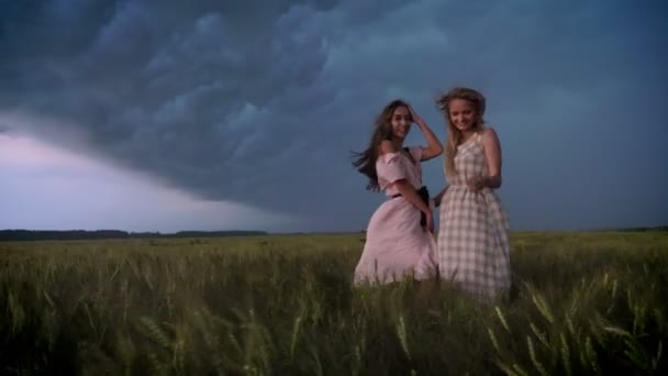 两个年轻迷人的女孩穿着连衣裙是 enjoing 风在田野里在雨天, 自由的概念, 调情的概念 — 图库视频影像