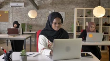 Dizüstü bilgisayarda yazarak ve esneme, hijab genç Afrika Müslüman kadınları sıkılmış, modern ofisinde çalışan üç güzel Müslüman kadın