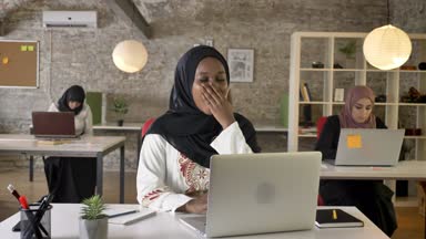 Dizüstü bilgisayarda çalışan ve esneme, hijab genç siyahi Müslüman kadınları yorgun, modern ofisinde oturan üç güzel Müslüman kadın