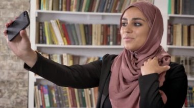 Genç Müslüman güzel kadınlar türban alarak selfie sonra telefon görünümlü ve Fotoğraf Kitaplığı ' nda izlerken portresi gülümseyen