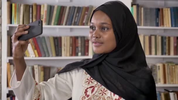 Jeunes femmes musulmanes noires en hijab prenant selfie puis regardant le téléphone dans la bibliothèque, souriant, étudiant musulman africain — Video