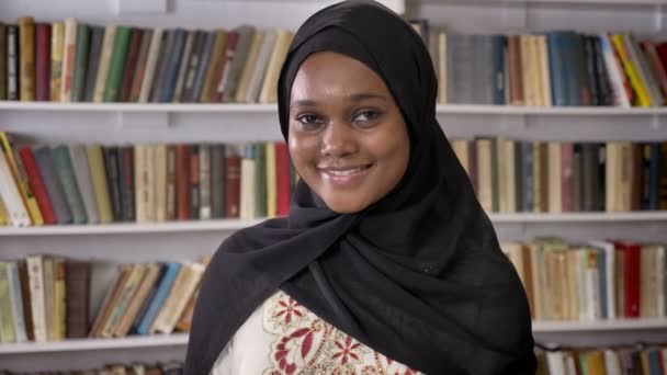Портрет молодих красивих африканських мусульманських жінок в хіджабі, які дивляться в камеру і посміхаються, стоячи в бібліотеці — стокове відео