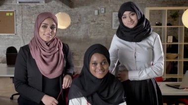 Üç genç Müslüman kadın kamera seyir ve modern ofiste gülümseyen hijab içinde iş ekibi