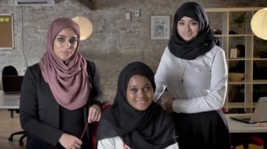 Üç genç Müslüman kadın kamera seyir ve modern ofiste Siyahi Müslüman kadınlar İşyerinde meslektaşları ile gülümseyen hijab içinde